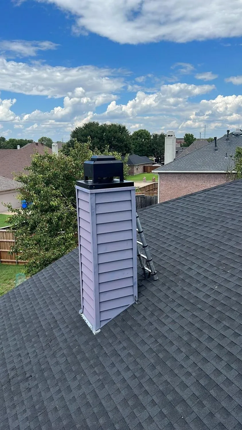 Blue sided chimney with black cap on gray shingle roof