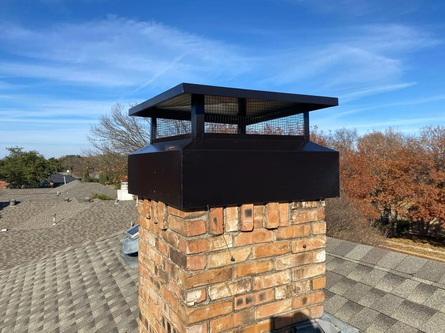 Brick chimney with new black cap on roof under blue sky