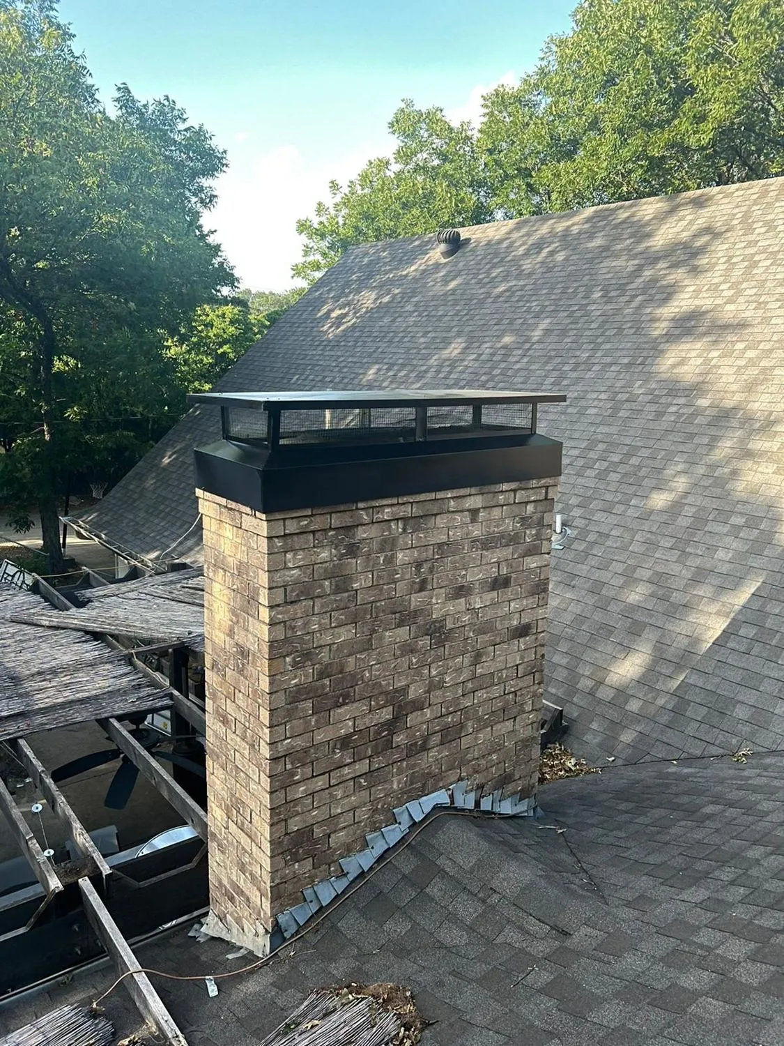 Brick chimney with black cap on shingle roof