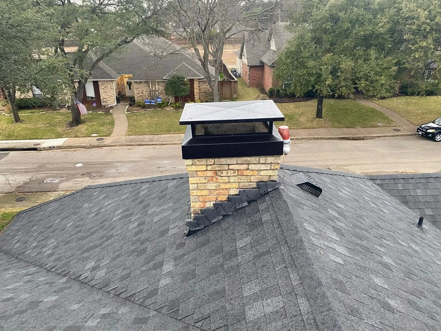Brick chimney with a new black cap seen across a shingle roof