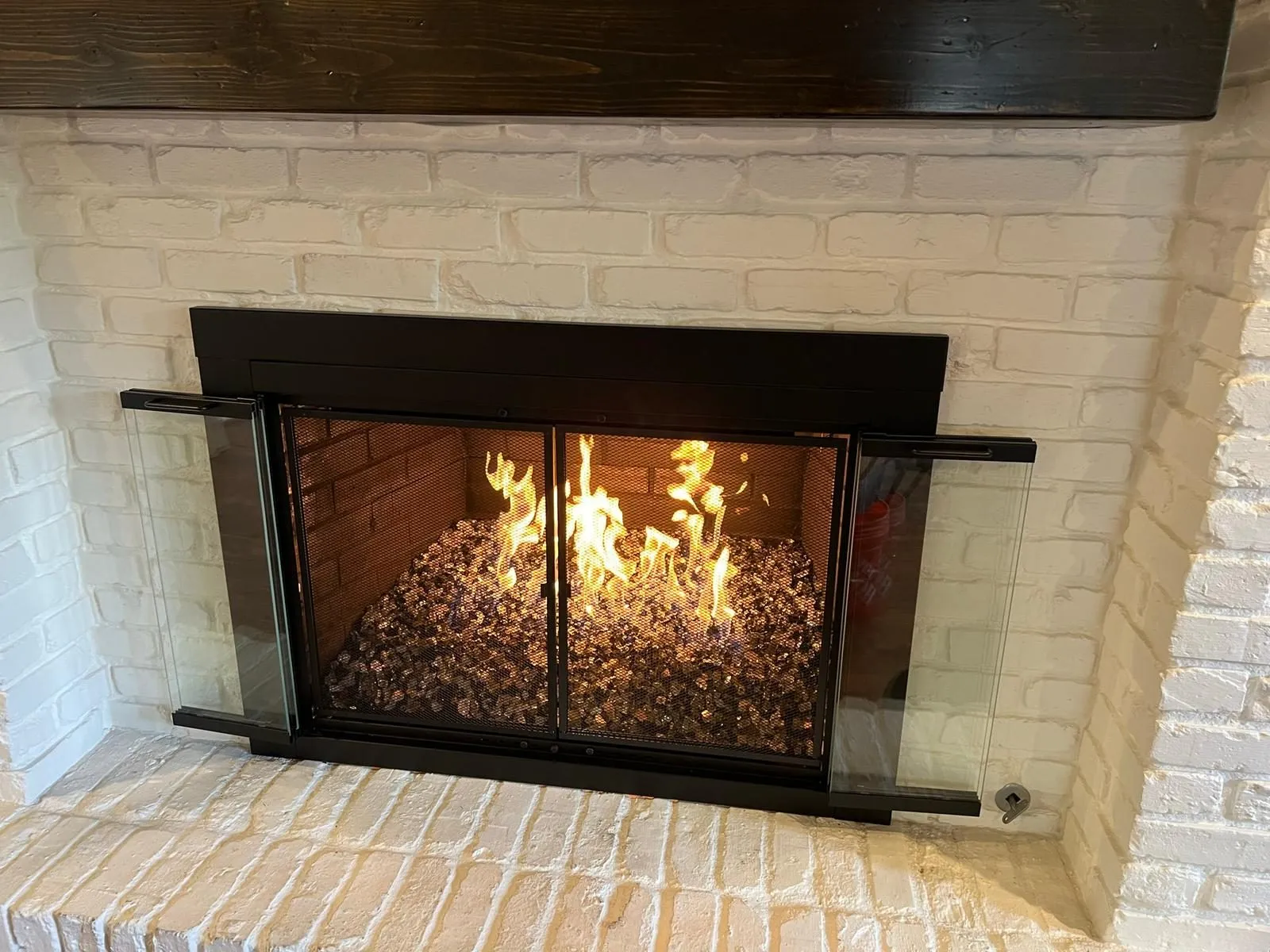 Flames burning behind black glass doors of white brick fireplace