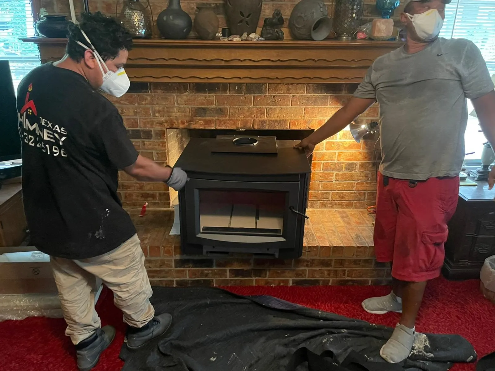 Workers positioning black insert into brick fireplace