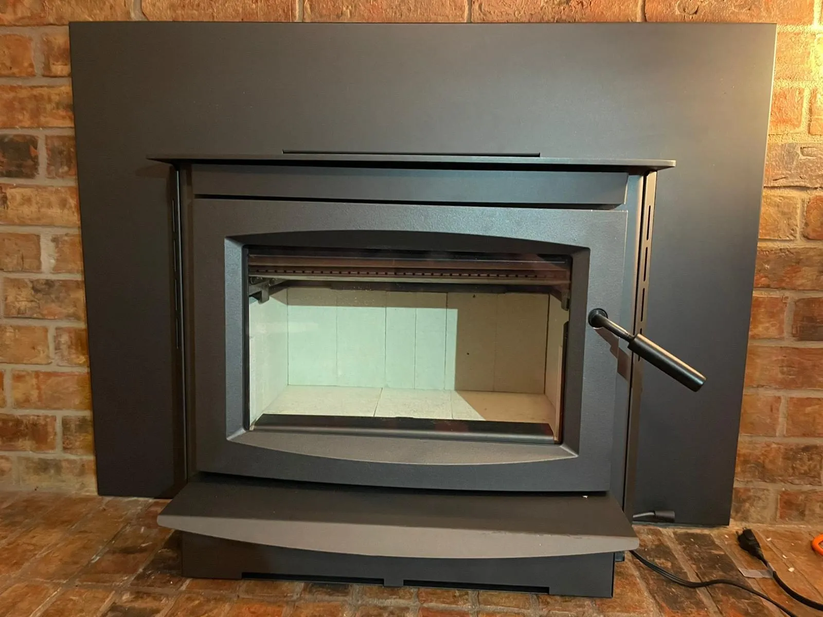 New black fireplace insert installed in brick opening