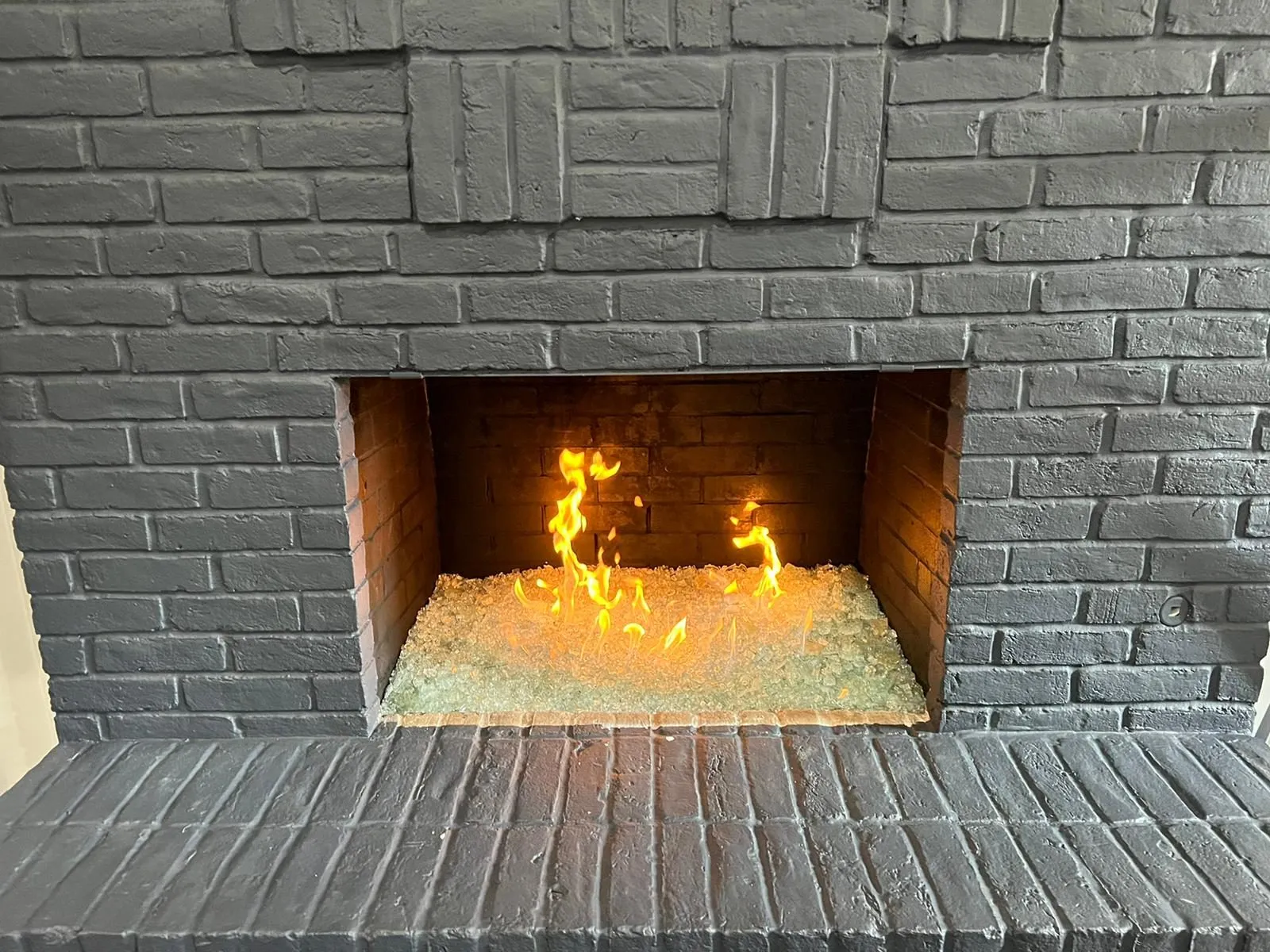 Gas flames on glass media inside gray painted brick fireplace