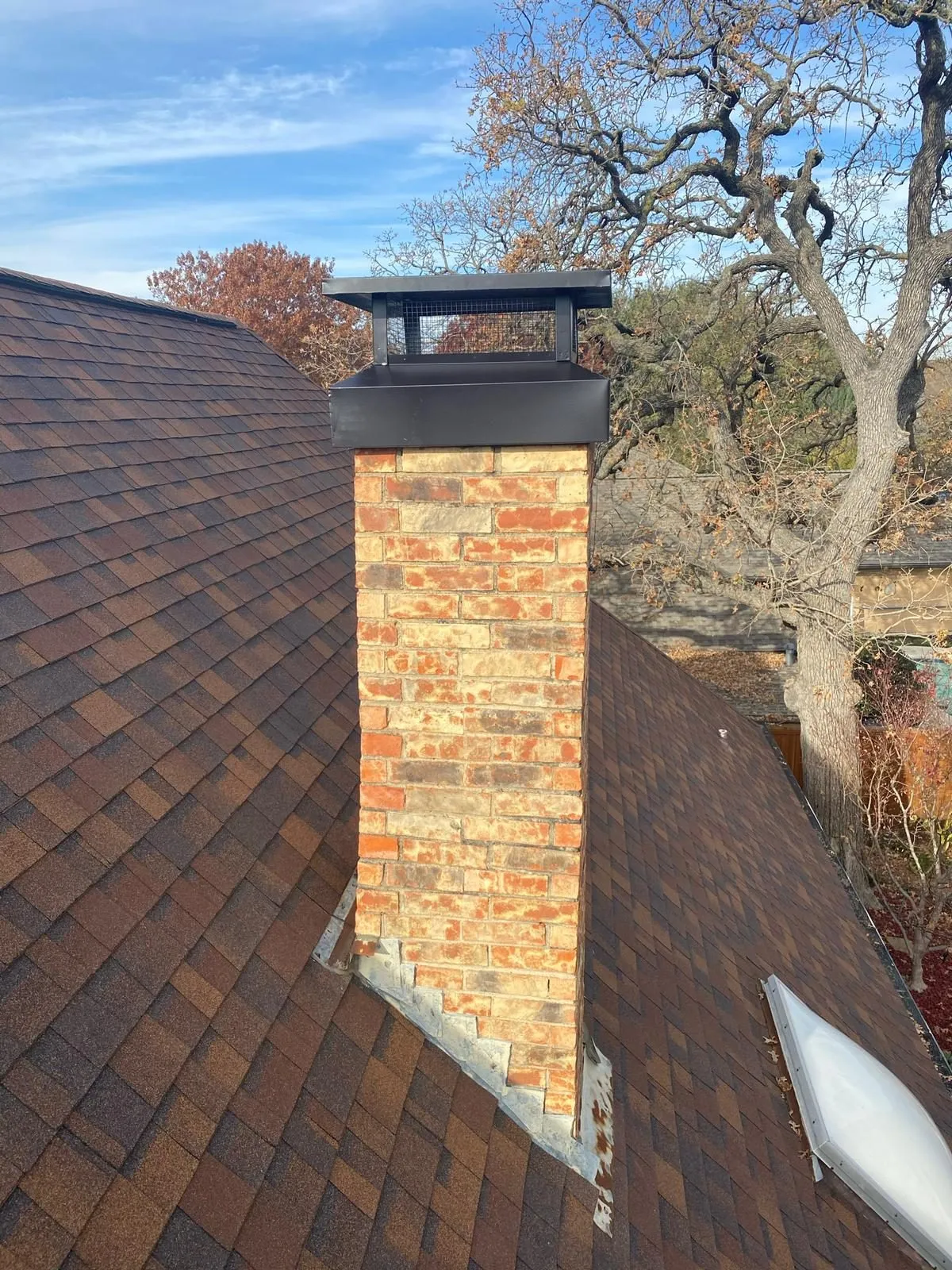 Red brick chimney with black cap surrounded by autumn trees