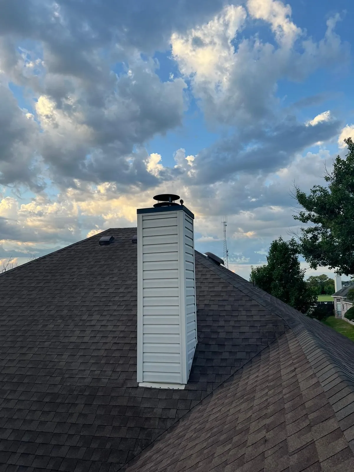 White sided chimney on dark shingle roof under dramatic clouds