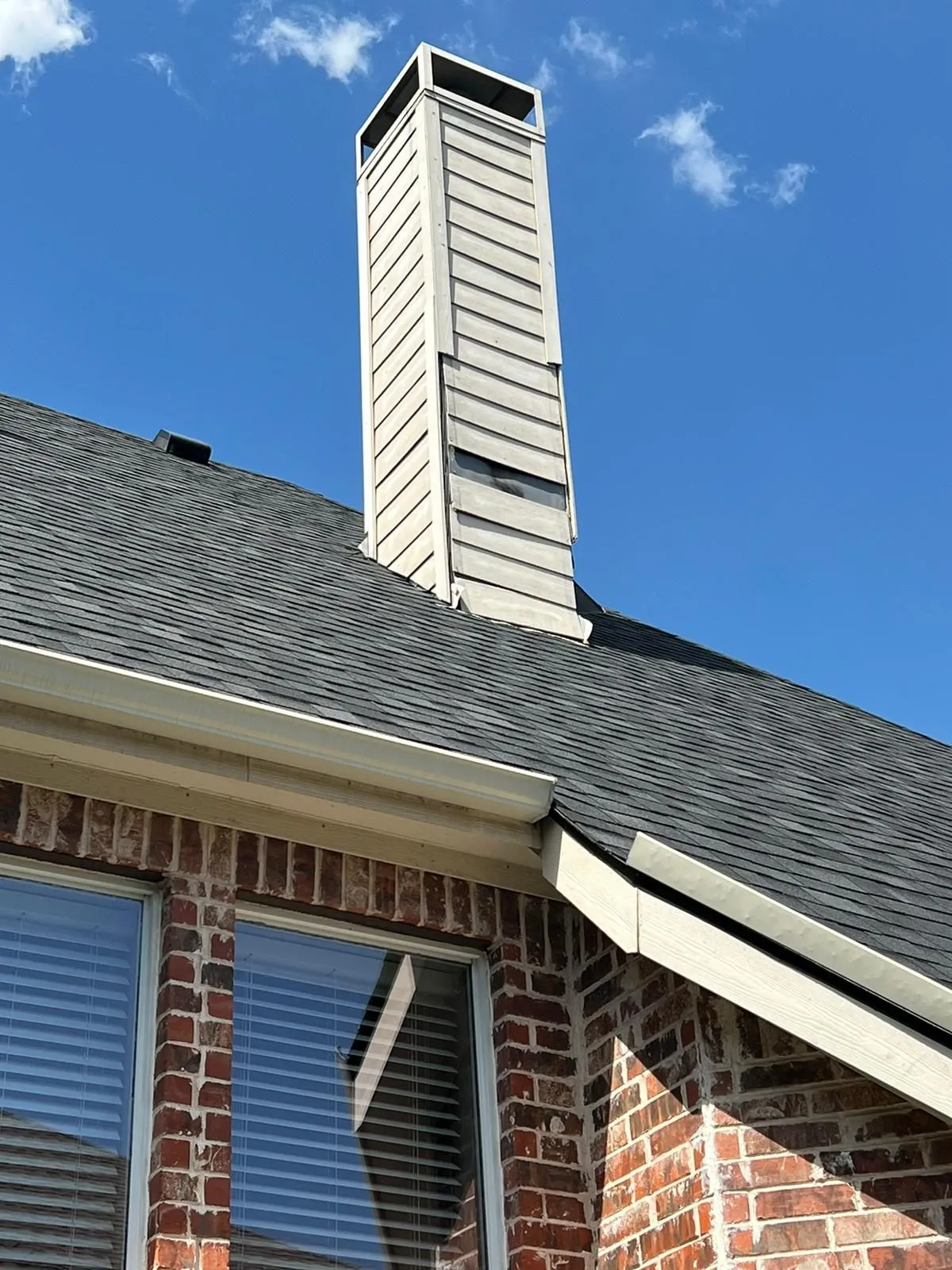 Tall sided chimney towering over brick home against blue sky